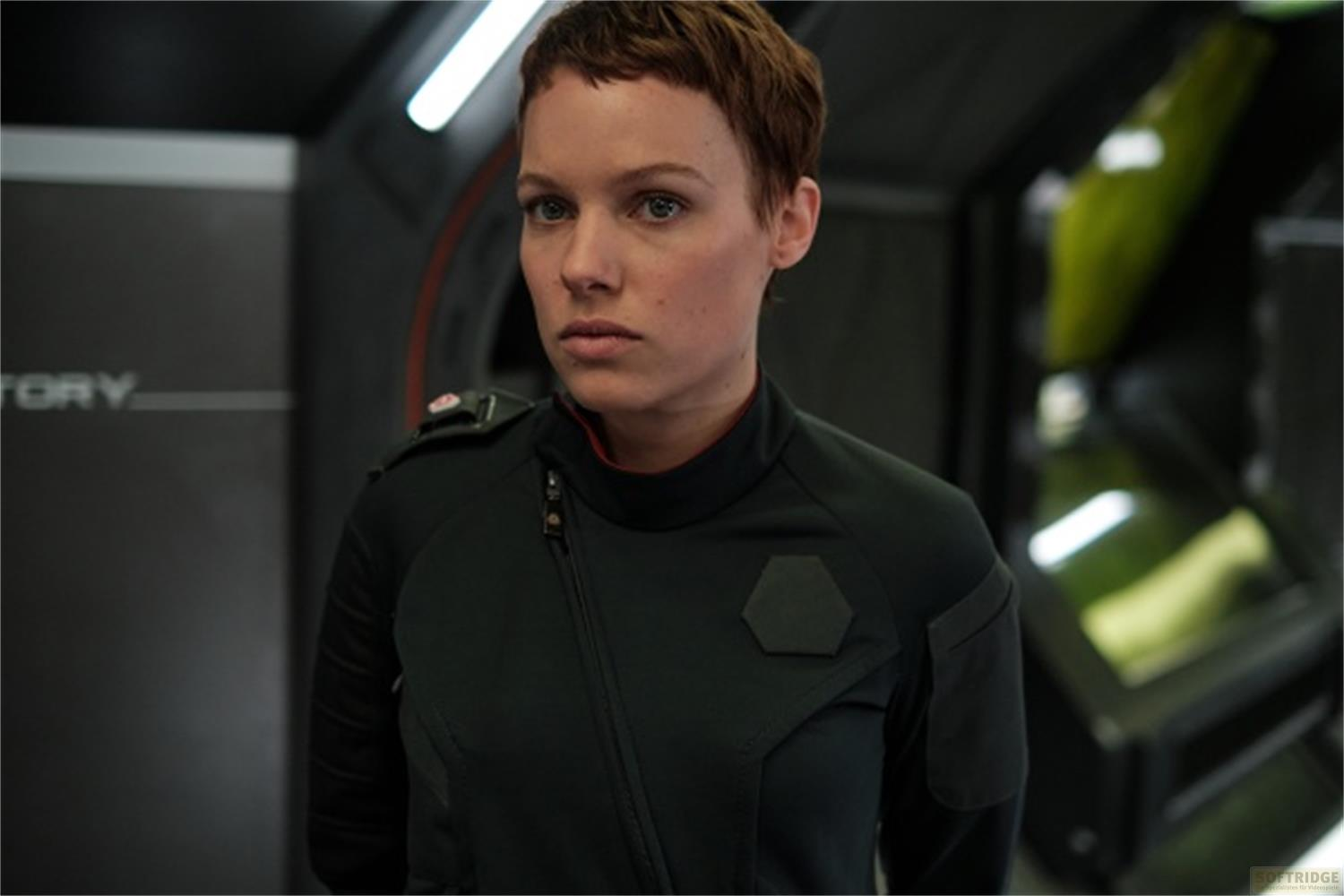 Una donna con capelli castani corti indossa un'uniforme nera in una stanza buia.