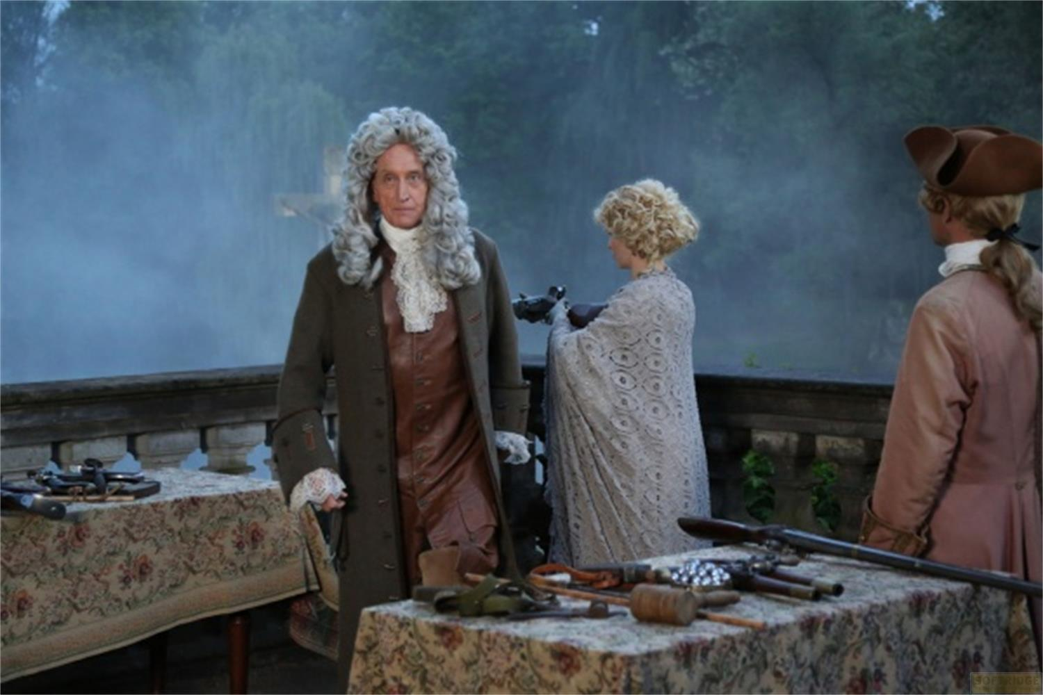 Uomini e donne in costume storico stanno su una terrazza con armi sui tavoli.