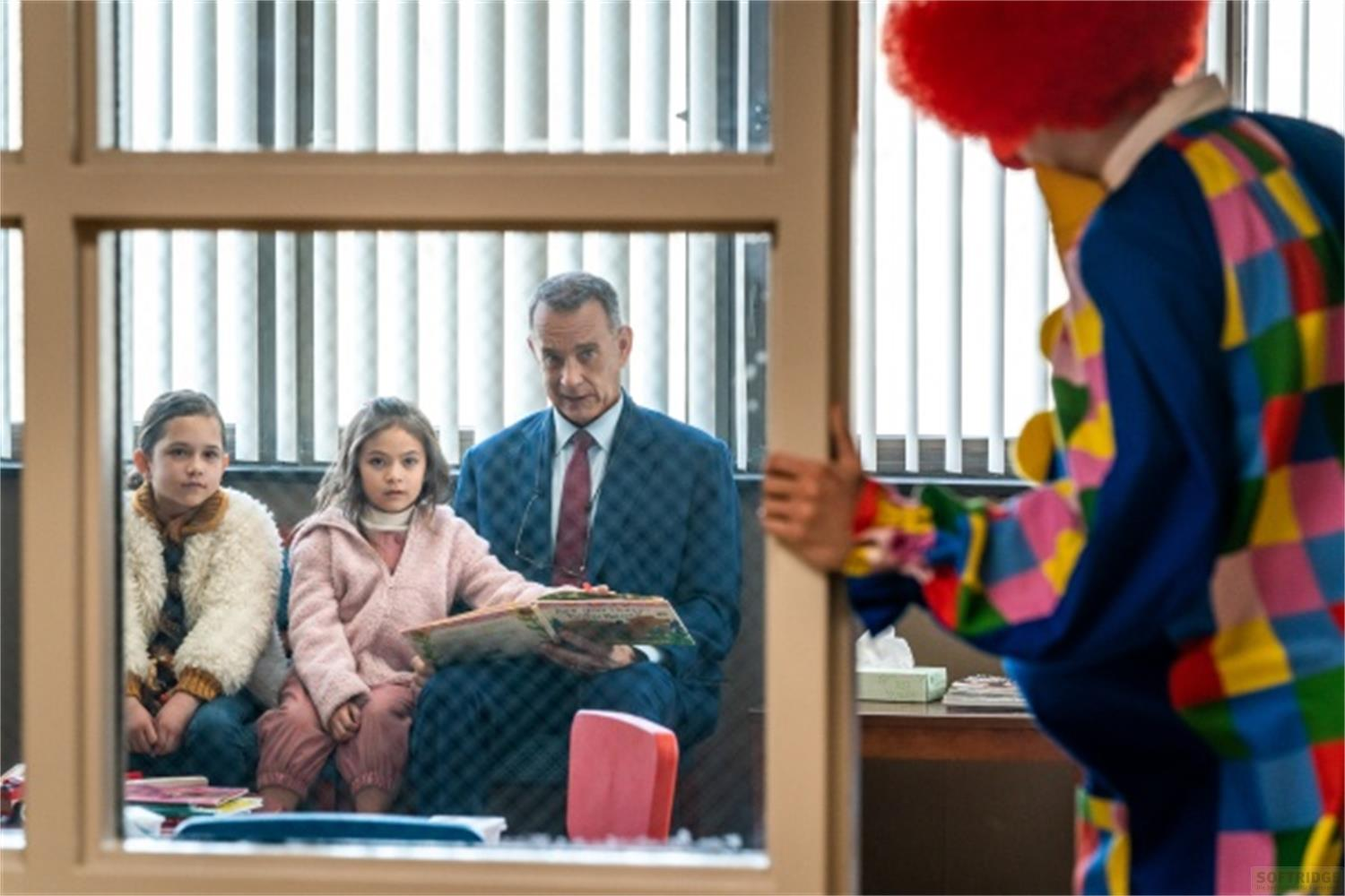 Uomo in abito legge ai bambini; un clown entra a destra.