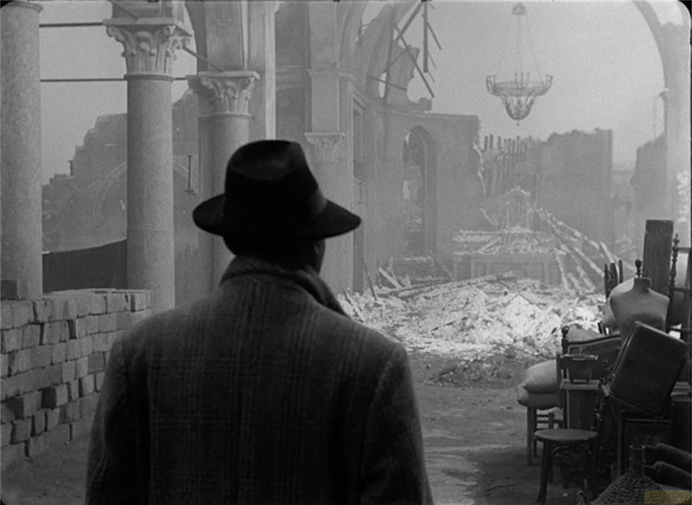 Uomo con cappello davanti a chiesa in rovina con detriti e lampadario.