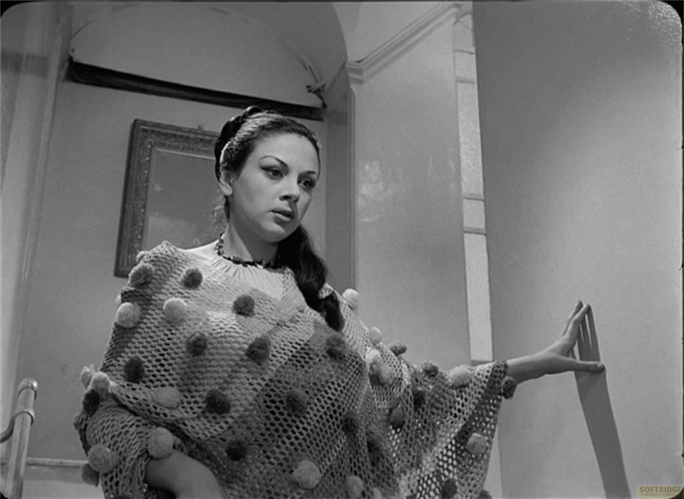 Una donna con un poncho adornato di pompon si appoggia a un muro.