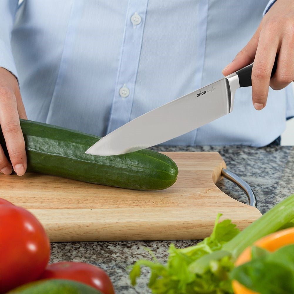 Una persona con camisa azul corta un pepino en tabla de cortar de madera con cuchillo.