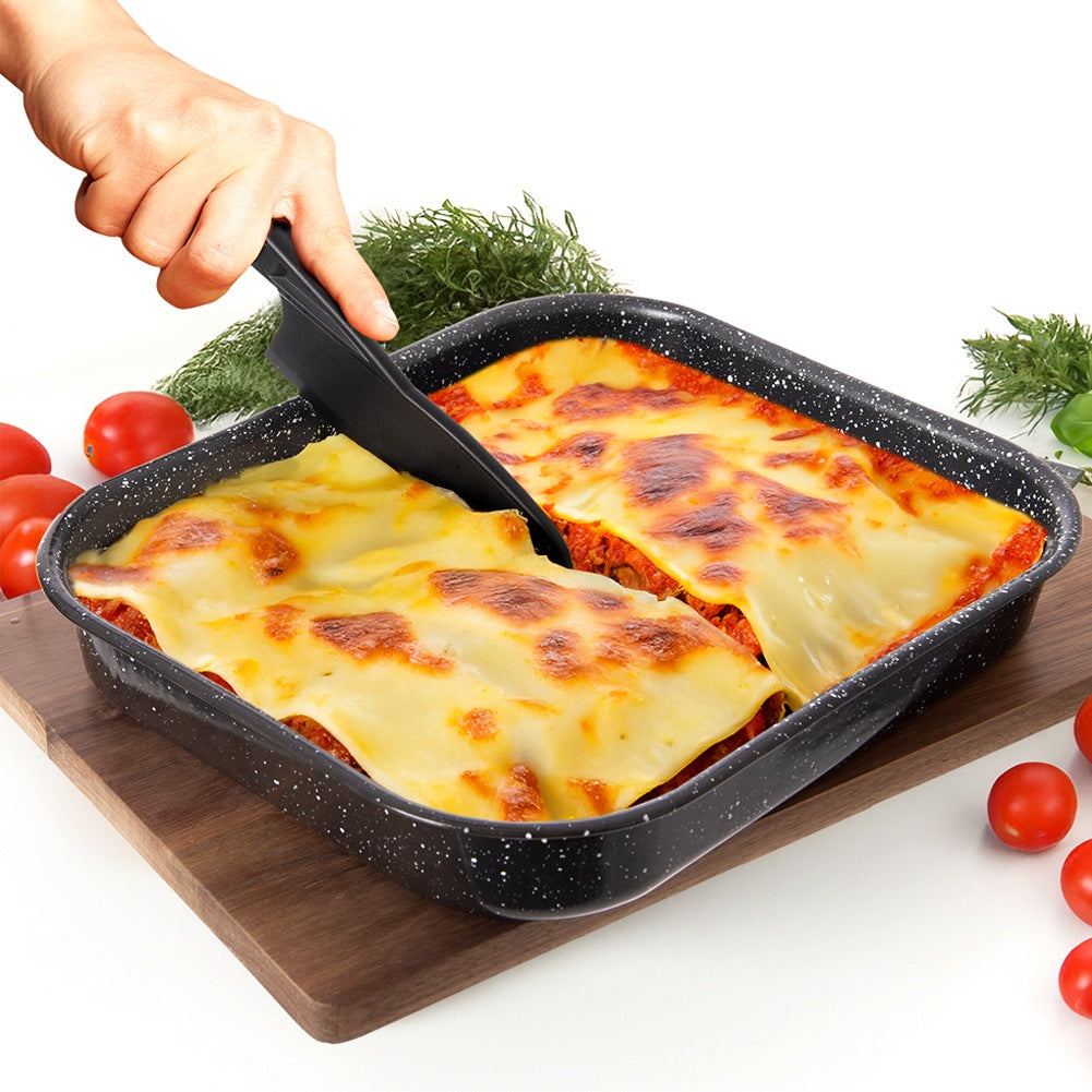 Una mano usa una herramienta negra para cortar lasaña en una bandeja de horno negra moteada.