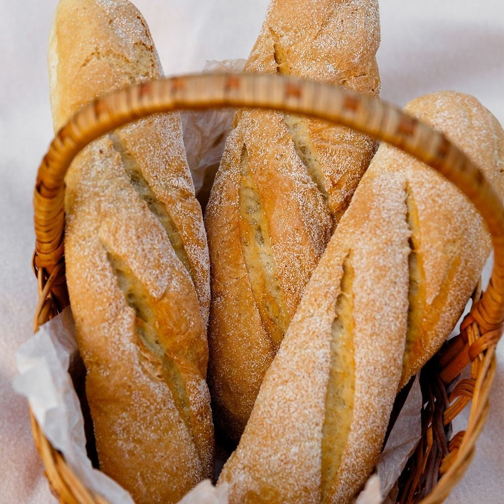 Una cesta tejida con cuatro baguettes doradas, ligeramente espolvoreadas con harina.