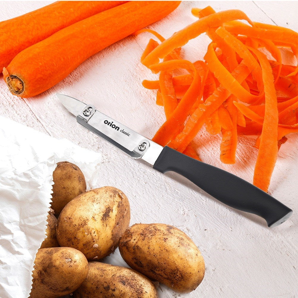 Un pelador yuca junto a zanahorias peladas y patatas sobre mesa madera.