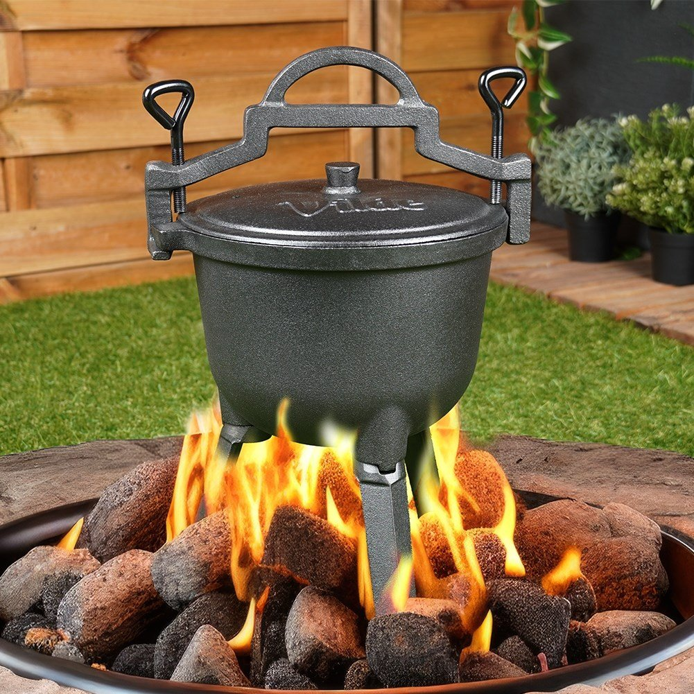 Una olla de hierro fundido con tapa se asienta sobre una hoguera con troncos y rocas encendidos.