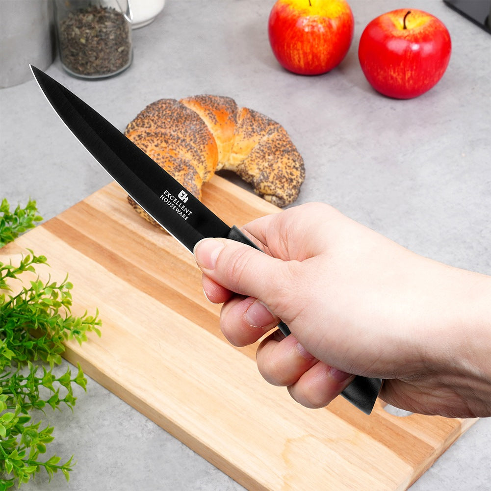 Mano sujetando un cuchillo negro sobre tabla de madera con pan y manzanas.