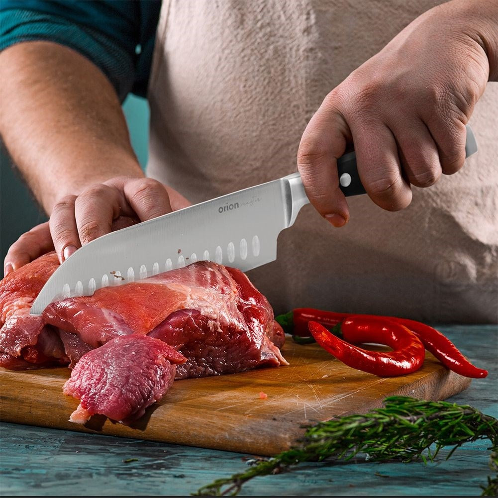 Un cocinero corta carne cruda en una tabla de madera con chiles y hierbas.