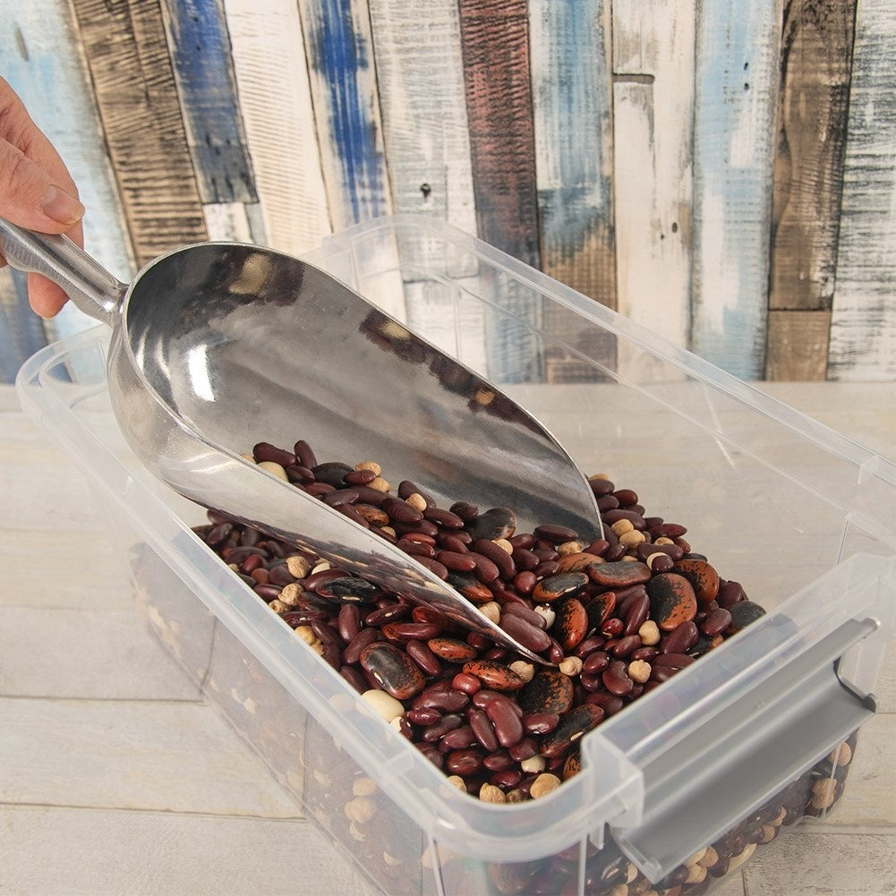 Una pala de metal levanta una mezcla de frijoles rojos y marrones de un recipiente de plástico.