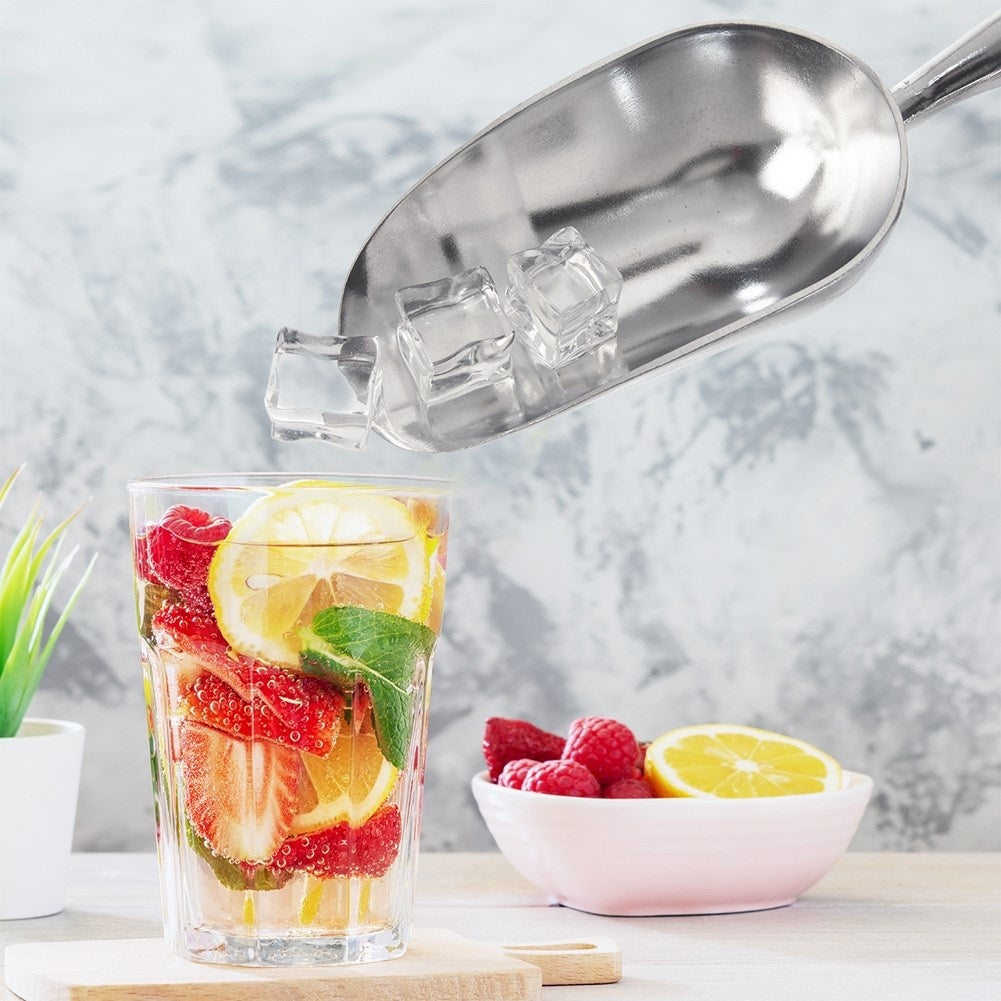 Una cuchara para hielo deja caer cubitos de hielo en un vaso con frutas.