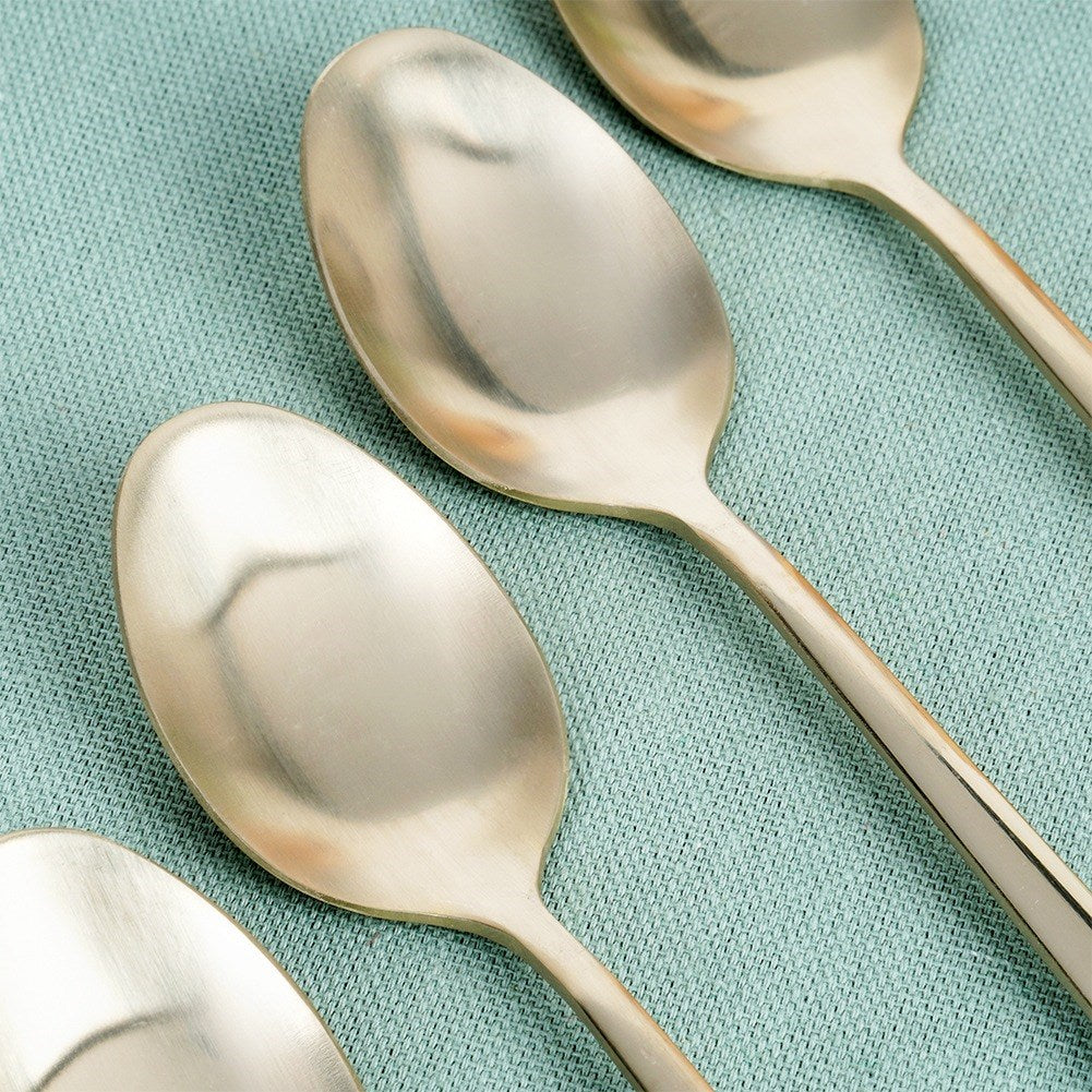 Varias cucharas doradas descansan sobre un paño azul claro.