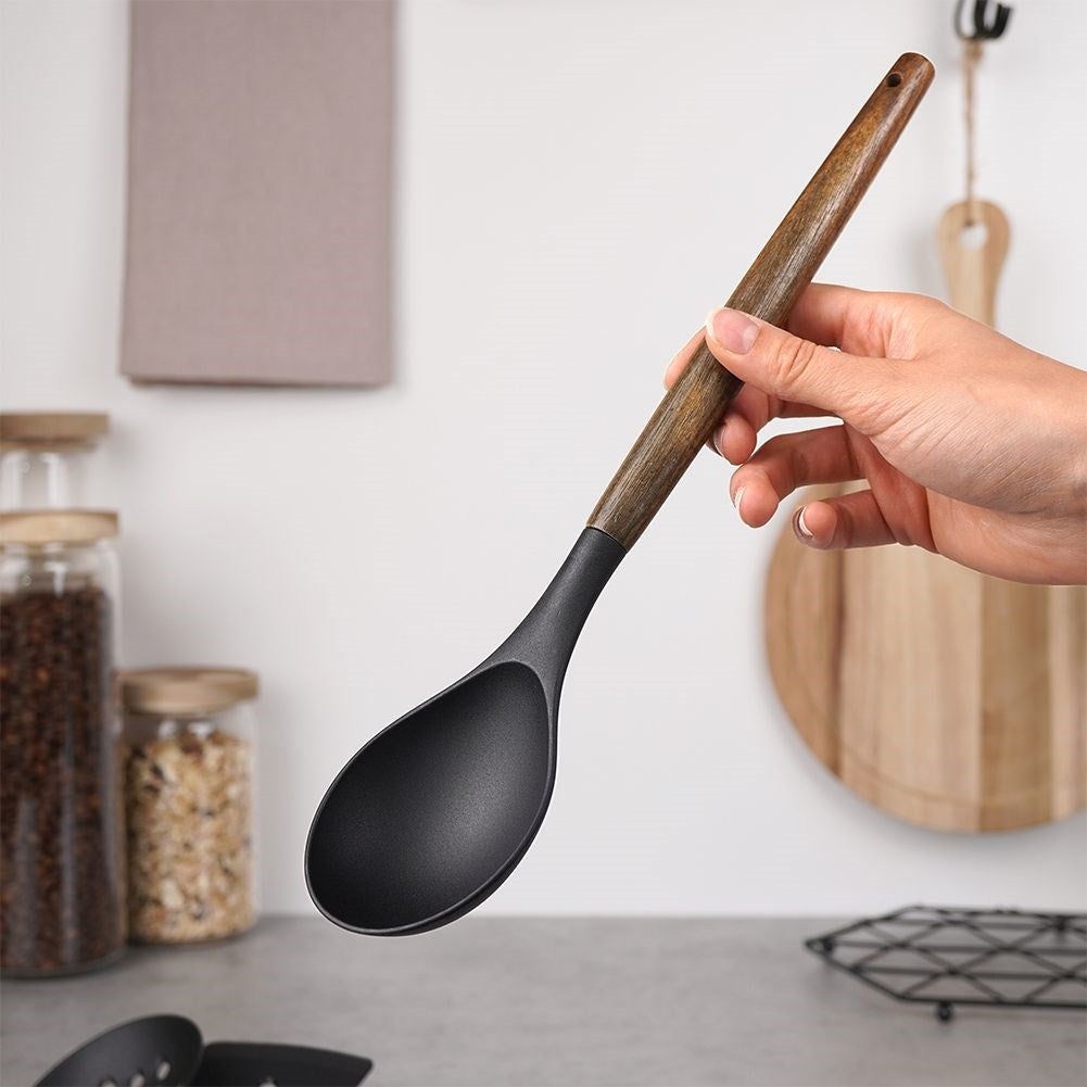 Una mano sostiene una cuchara negra con mango de madera frente a un fondo de cocina con frascos.