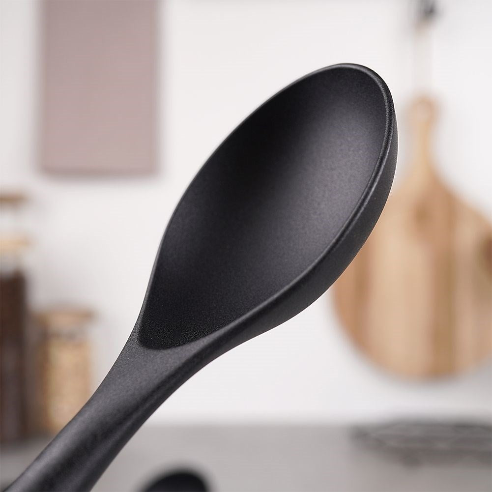 Primer plano de la punta de una cuchara negra sobre un fondo de cocina borroso.
