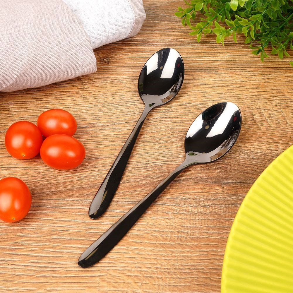 Dos cucharas negras sobre mesa de madera con tomates y hojas verdes.
