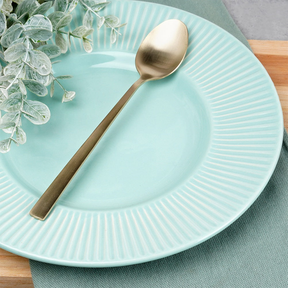 Una cuchara dorada sobre un plato azul claro acanalado.