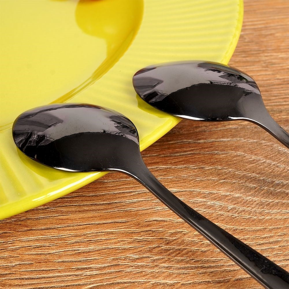 Dos cucharas negras descansan sobre un plato amarillo en una mesa de madera.