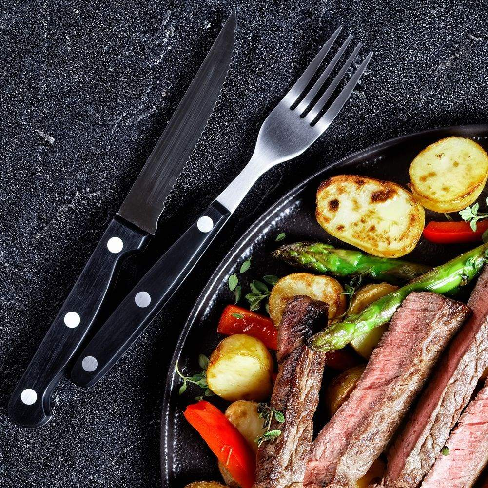 Un plato de bistec, patatas asadas, espárragos y pimientos, con cuchillo y tenedor.