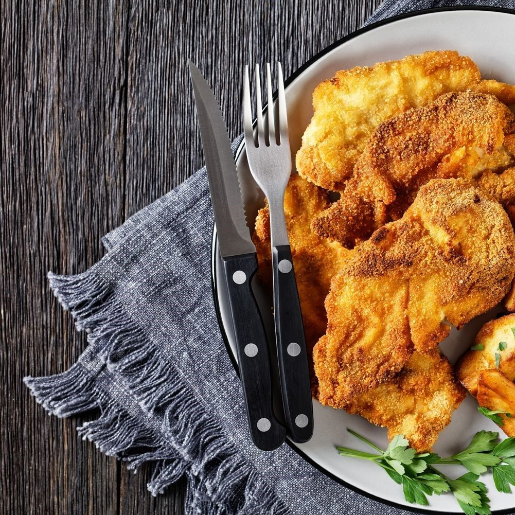 Chuletas fritas con cuchillo y tenedor en un plato con perejil, sobre fondo de madera.