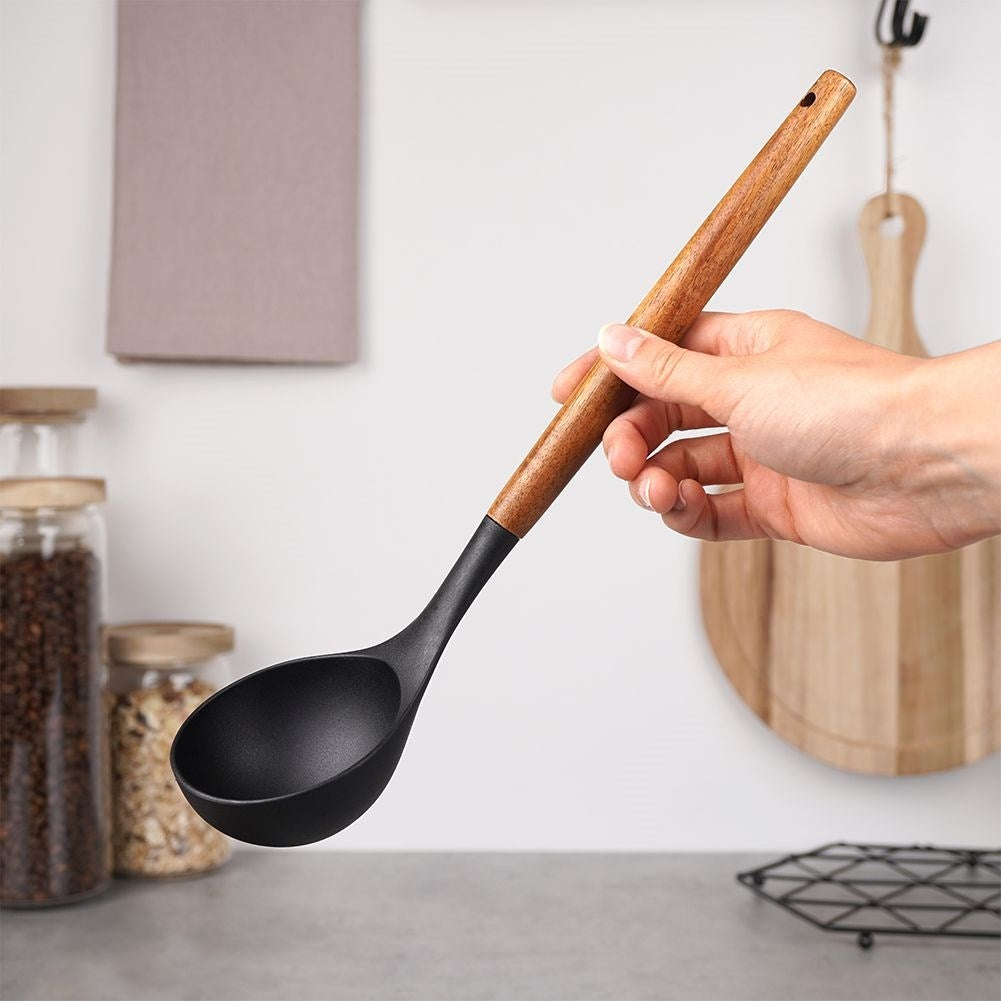 Una mano sostiene un cucharón negro con mango de madera frente a utensilios de cocina.