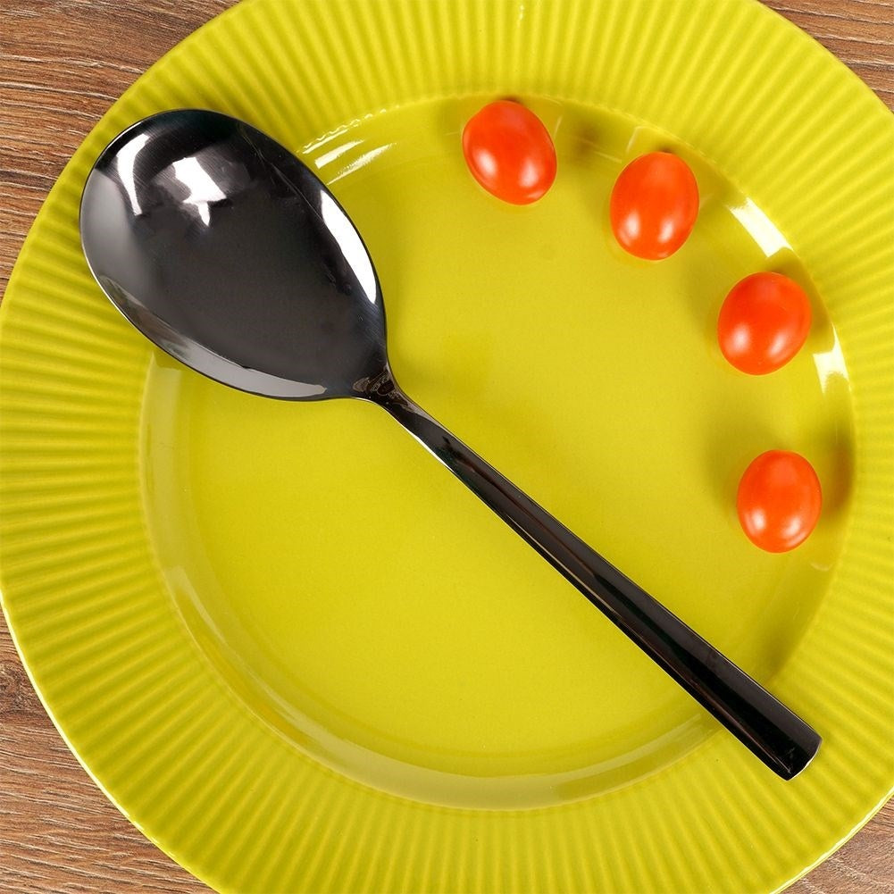 Una cuchara plateada y cuatro tomates cherry en un plato amarillo.