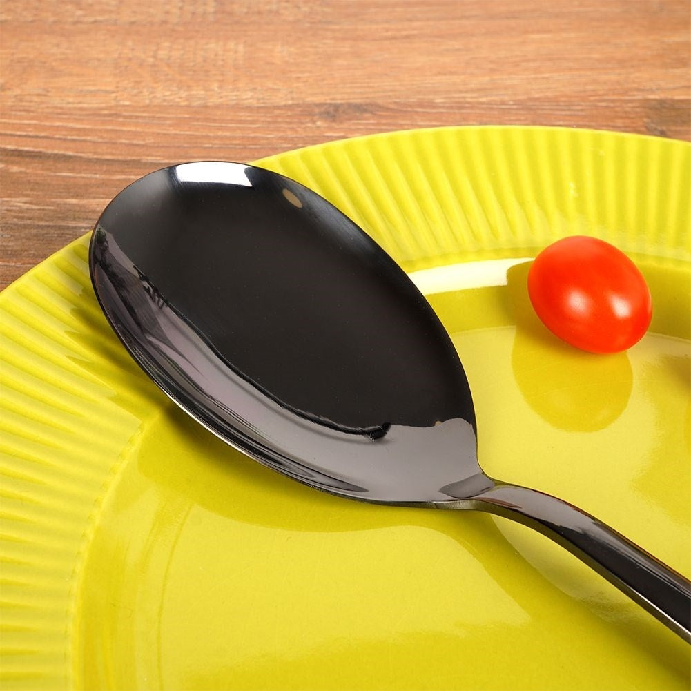 Una cuchara negra sobre un plato amarillo junto a un tomate.