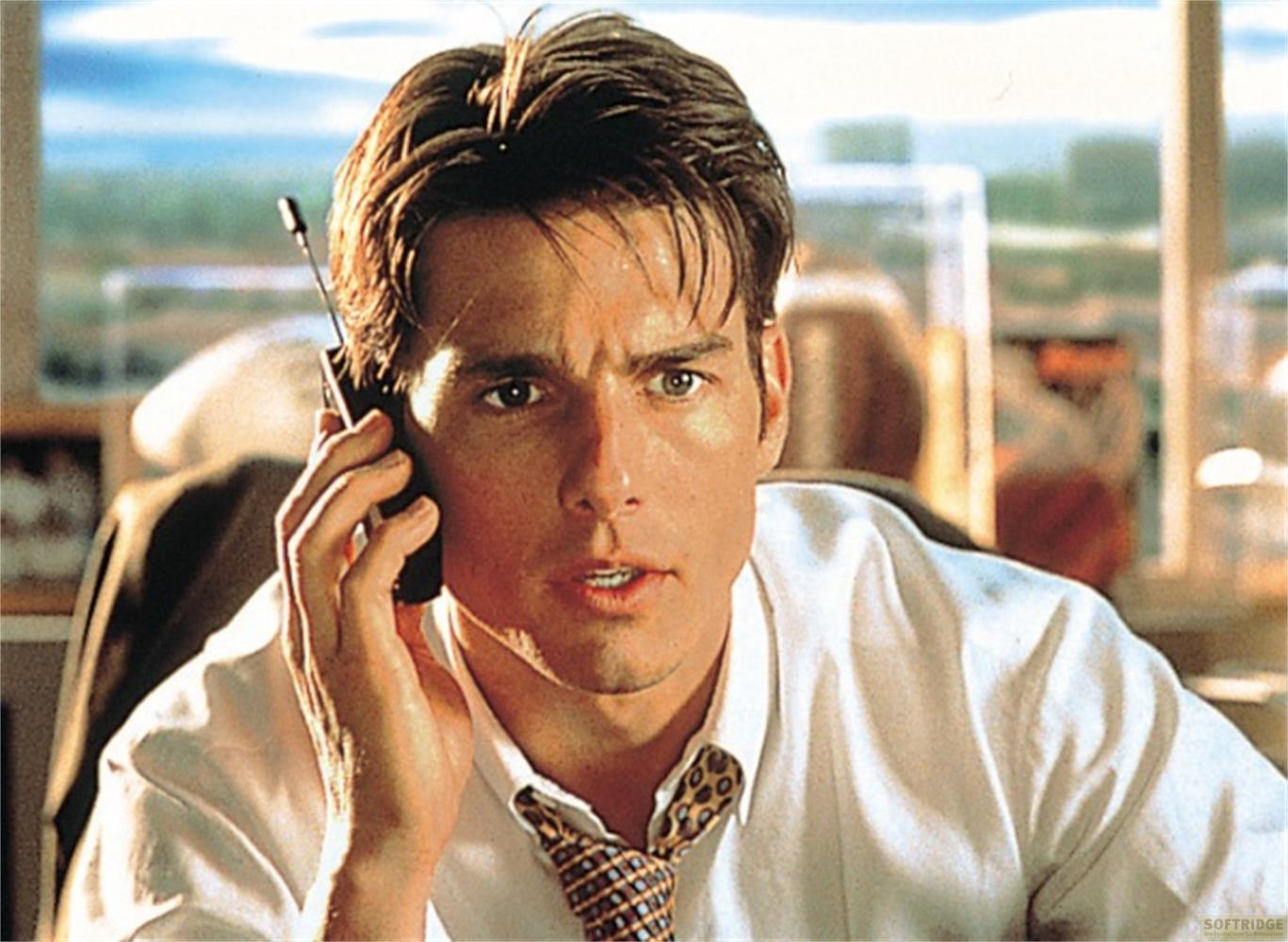Un uomo dai capelli scuri parla al telefono, indossa una camicia bianca e cravatta.