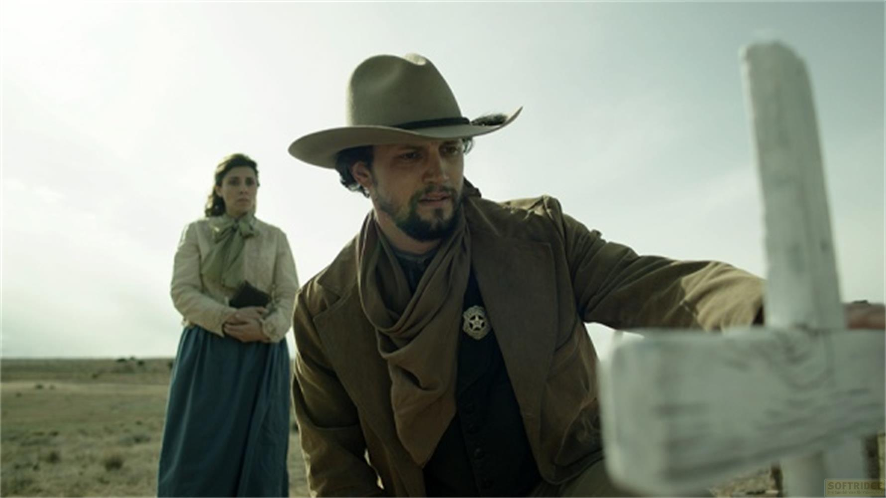 Un uomo con cappello da cowboy e una donna stanno all'aperto vicino a una croce.