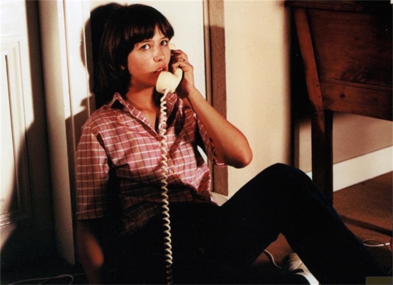 Una giovane donna seduta a terra parla al telefono beige.