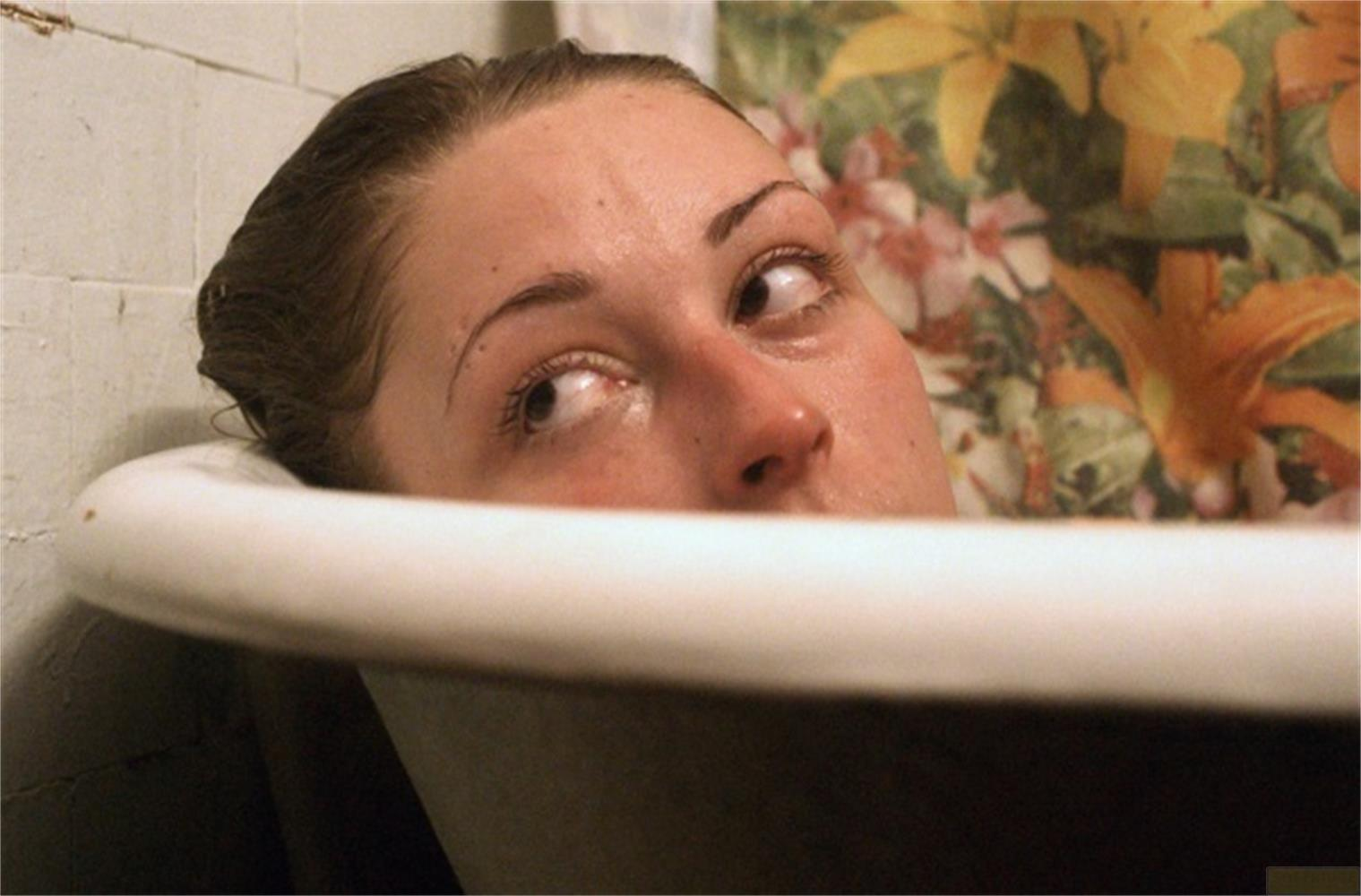 Donna in vasca da bagno, visibili solo occhi e naso, sfondo floreale.