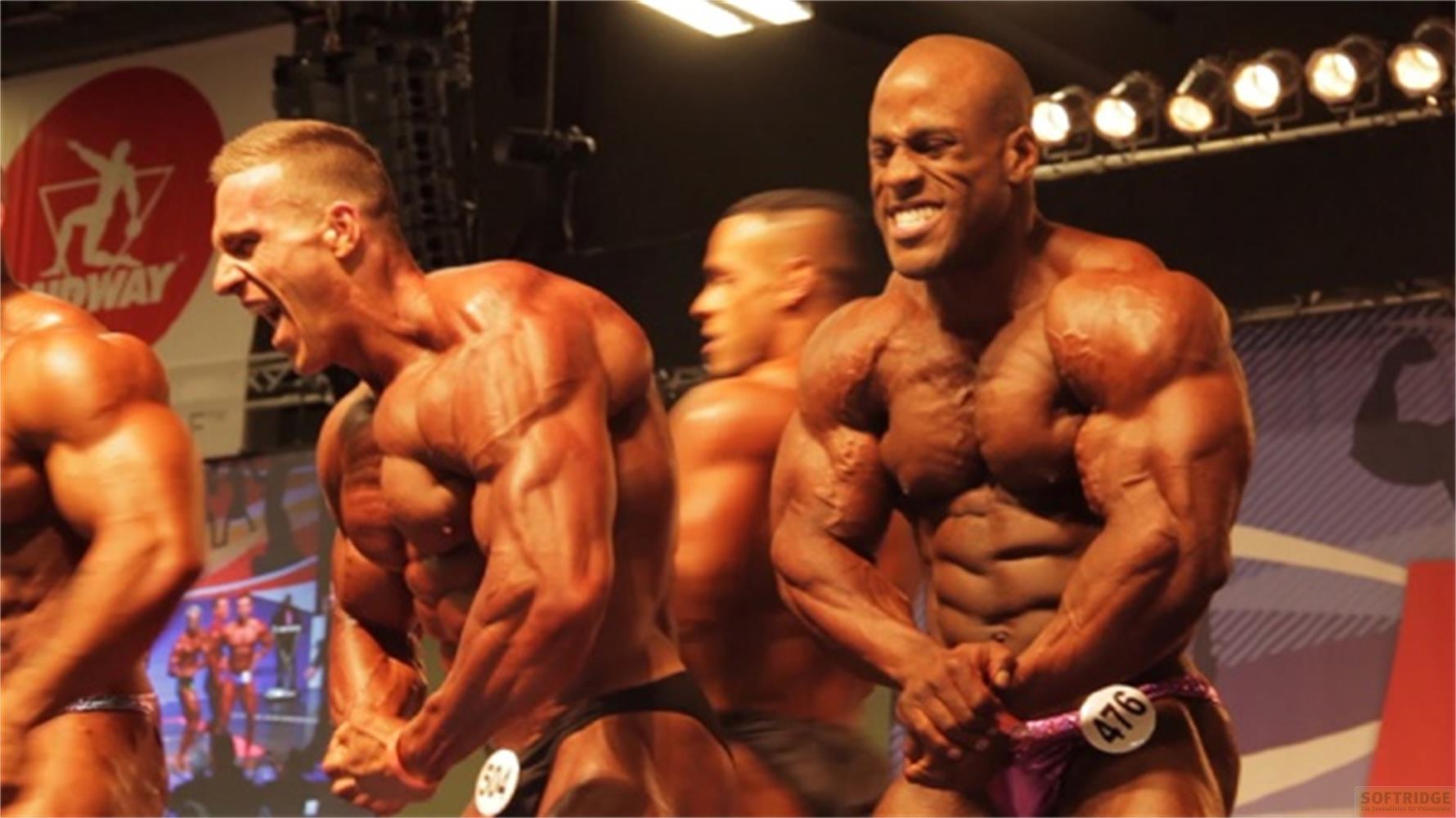 Bodybuilder in posa sul palco sotto i riflettori, con logo e luci.