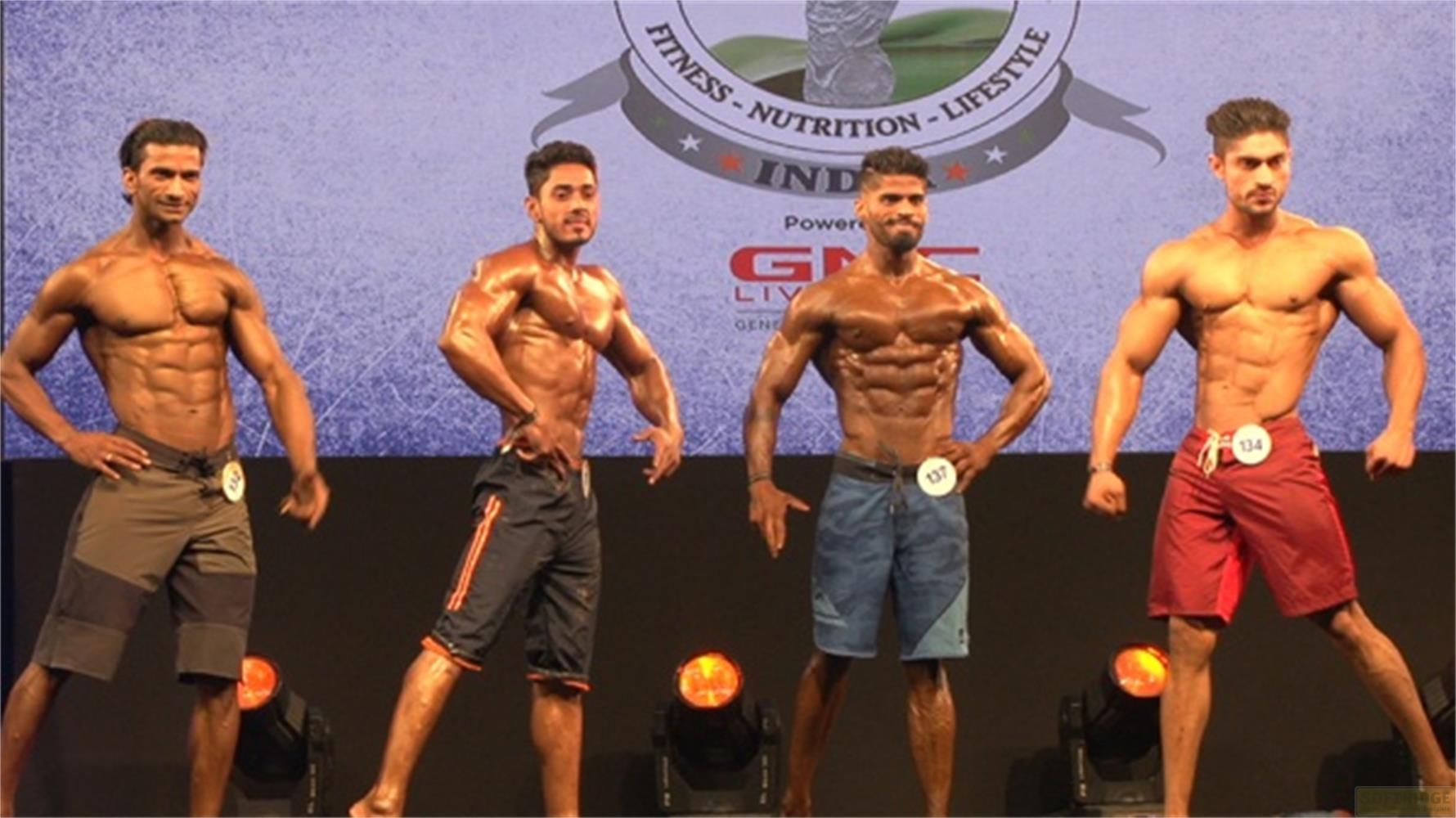 Quattro uomini muscolosi posano sul palco in costume da bagno. Fanno parte di una gara di bodybuilding.