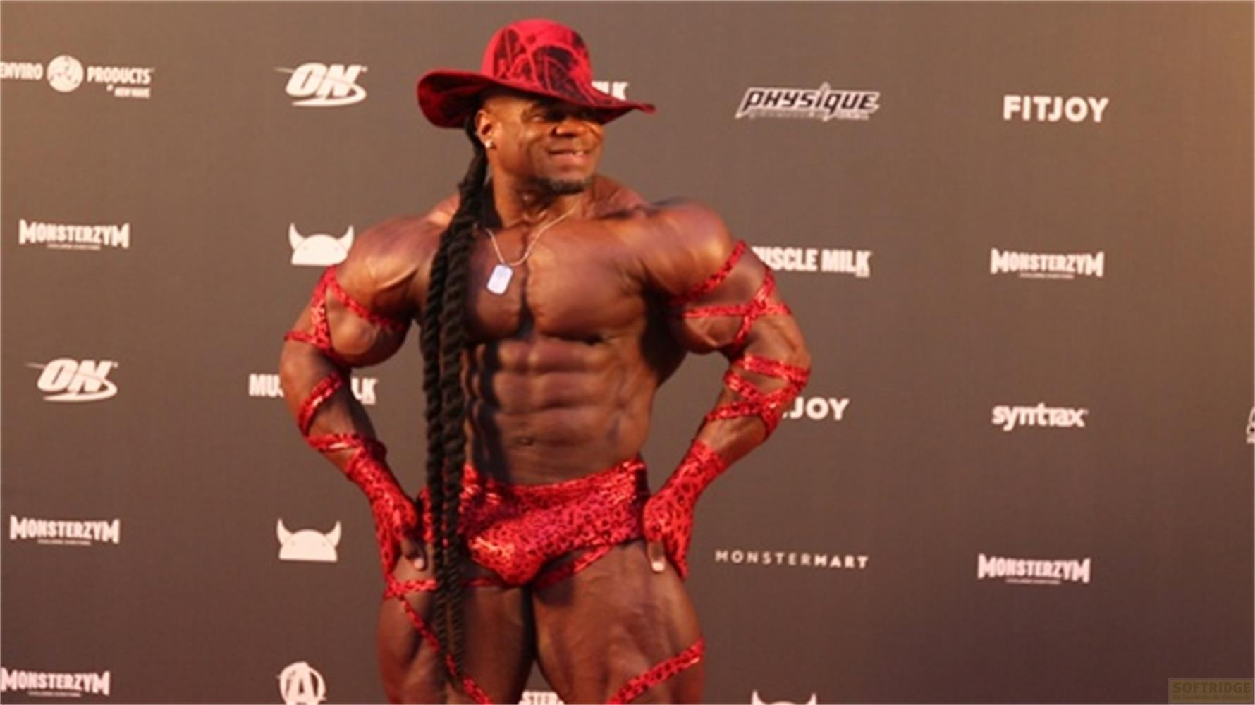 Un uomo muscoloso con cappello rosso e outfit leopardato posa.