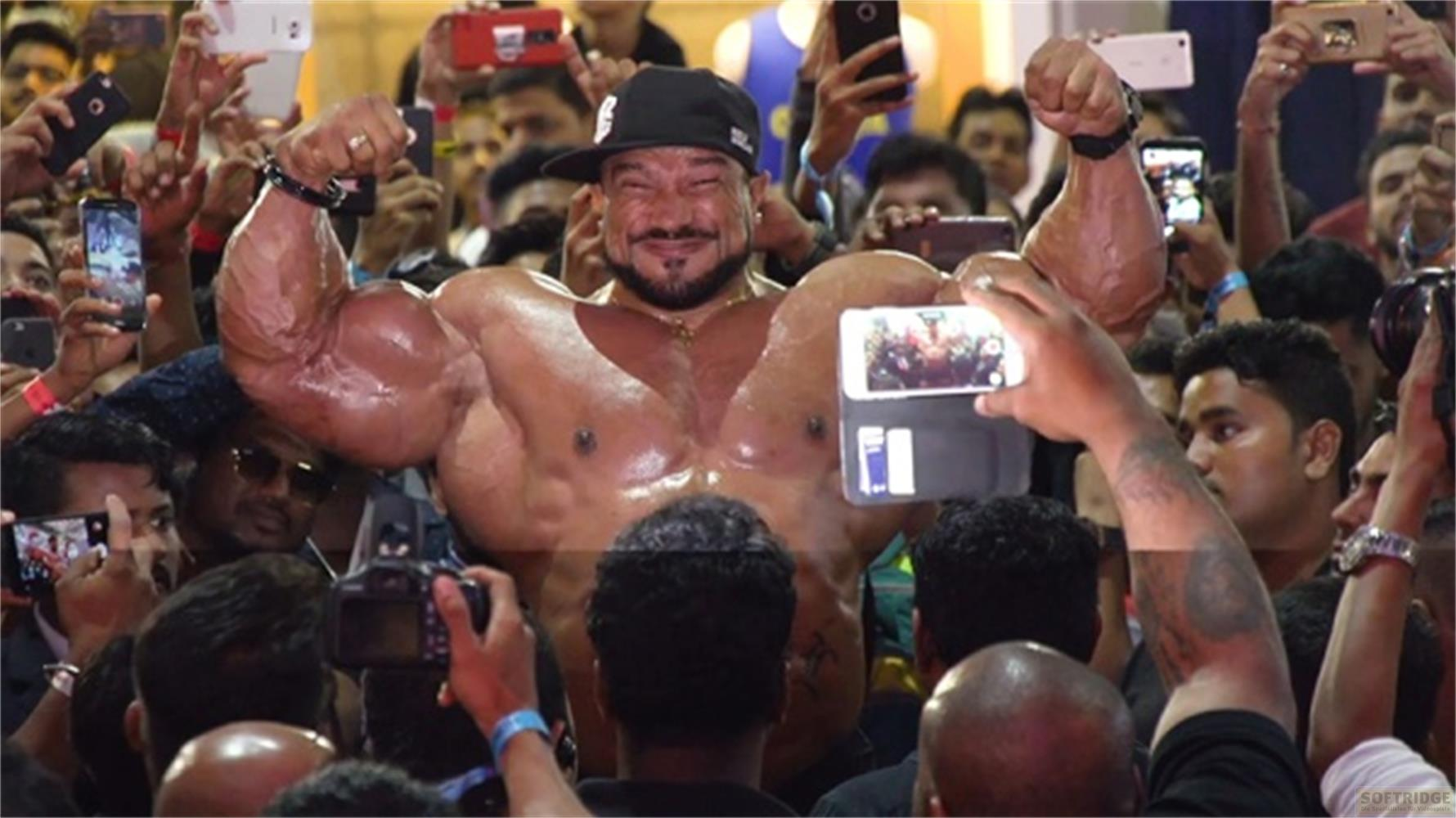 Un bodybuilder muscoloso posa per una folla che tiene molti telefoni.