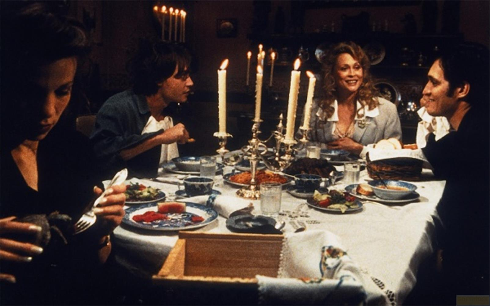 Quattro persone siedono a tavola a lume di candela, mangiando insieme.