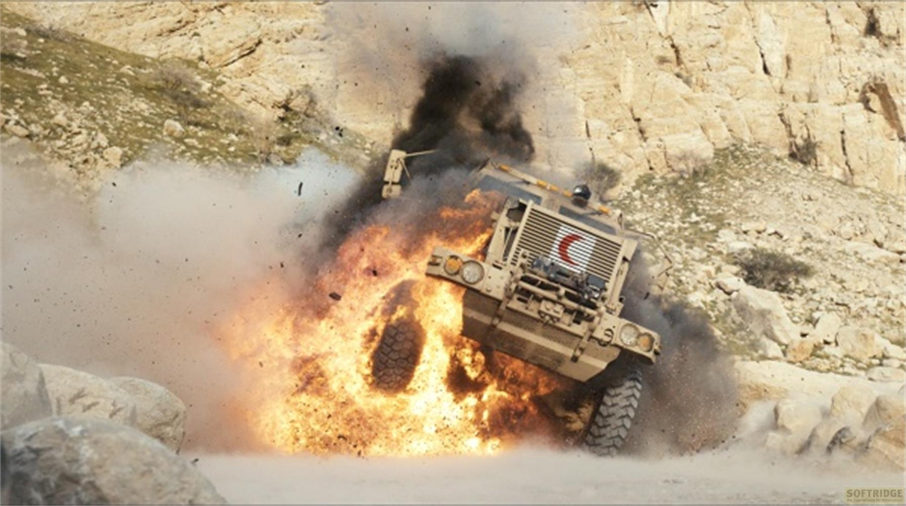 Un veicolo militare esplode in un paesaggio roccioso e polveroso.