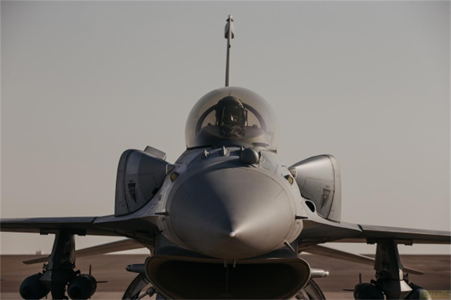 Un jet da combattimento grigio con pilota in cabina su una pista.