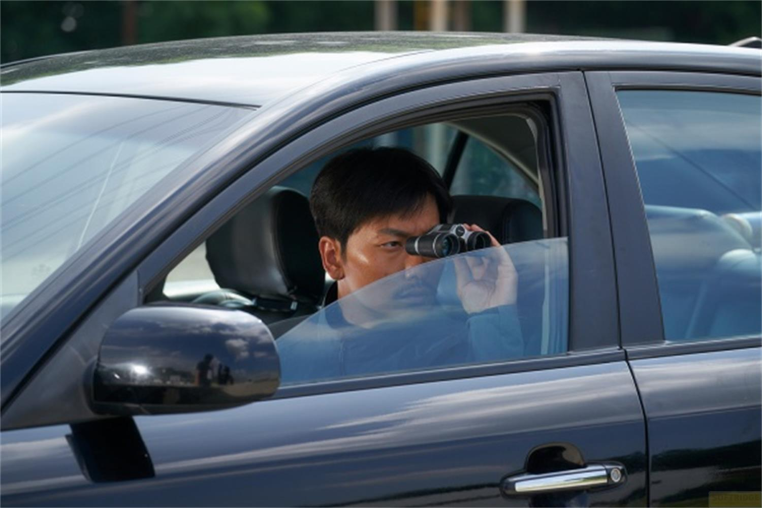 Uomo guarda attraverso un binocolo da dentro un'auto.