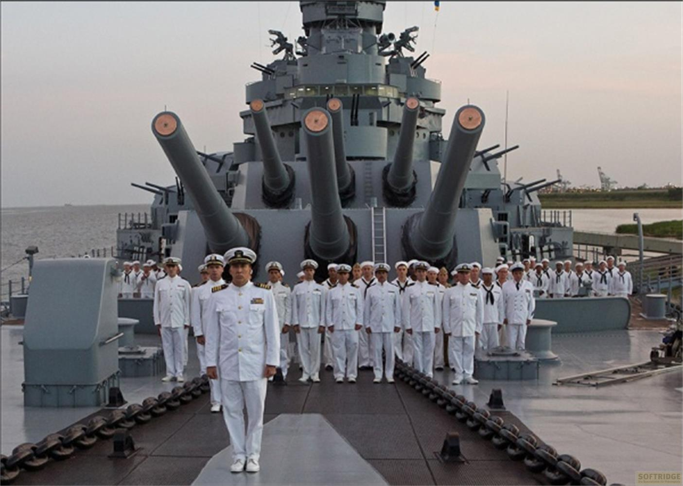 Des officiers de marine en uniforme blanc devant des tourelles de cuirassé.