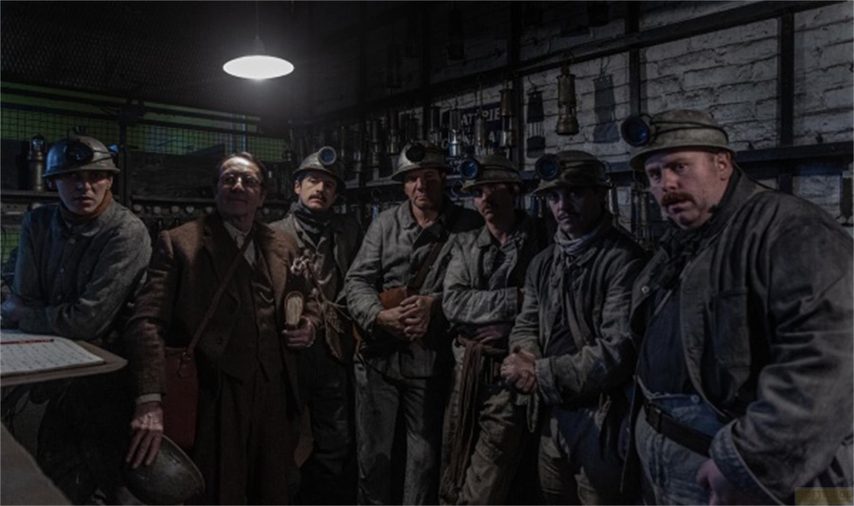 Sette minatori in abiti da lavoro e caschi stanno insieme in una stanza buia.