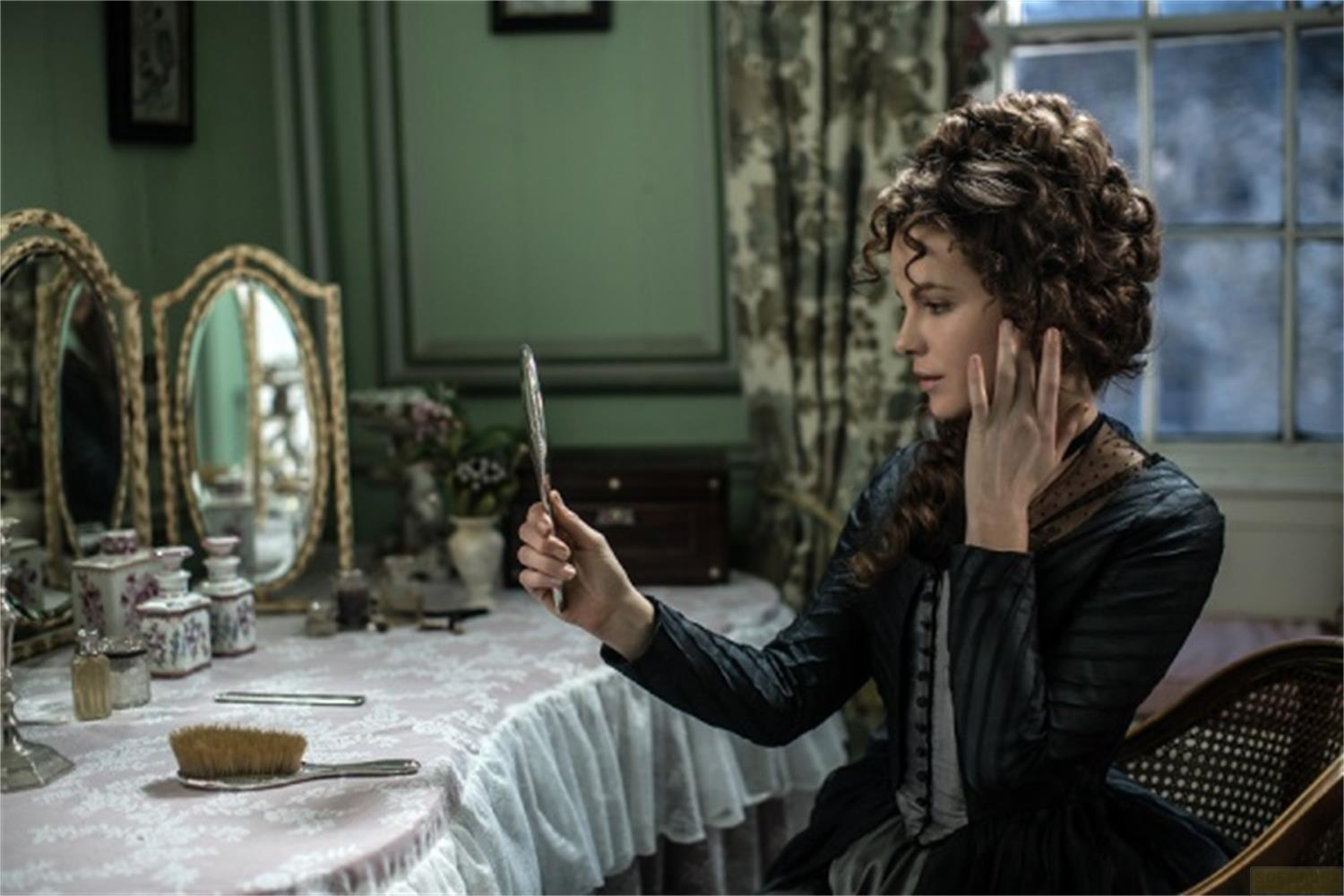 Una donna con capelli ricci si guarda in uno specchio a mano su un tavolino.