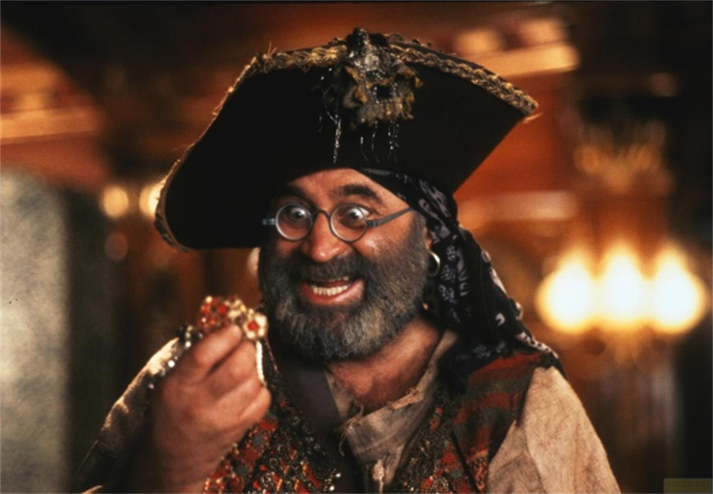 Un homme barbu et coiffé d'un chapeau tient des bijoux. Il porte un gilet.