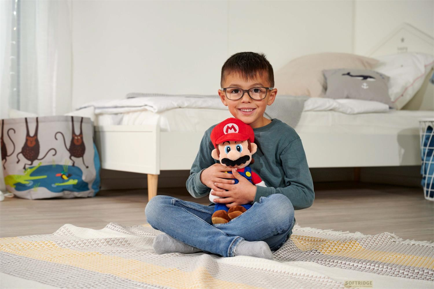 Ein Junge sitzt auf einem Teppich und hält eine Mario-Puppe. Im Hintergrund ein Bett und eine Spielzeugkiste.