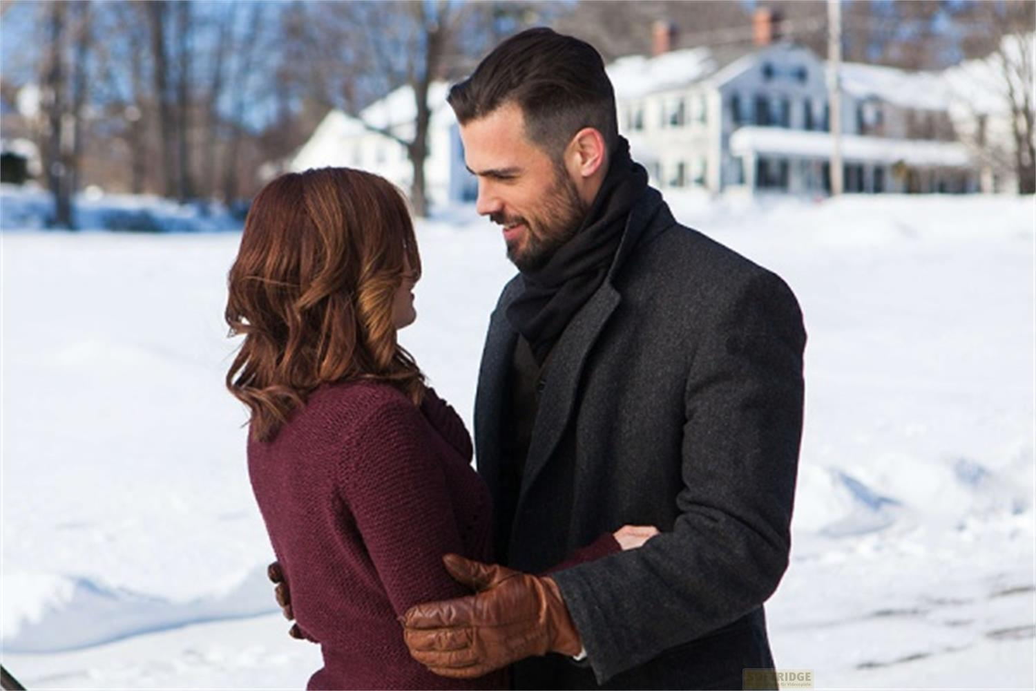 Un uomo e una donna si abbracciano nella neve, con case bianche.