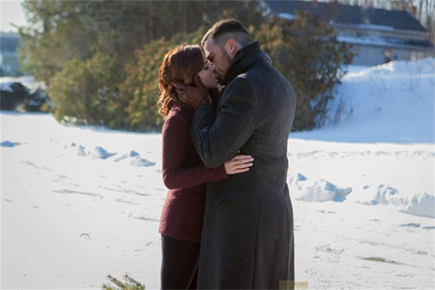 Una coppia si bacia sulla neve, una donna in bordeaux, un uomo in cappotto scuro.