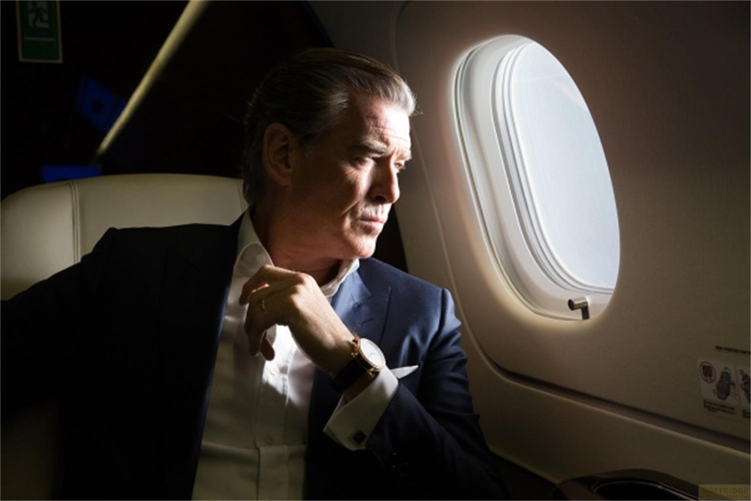 Un homme en costume sombre est assis dans un avion, regardant par le hublot.