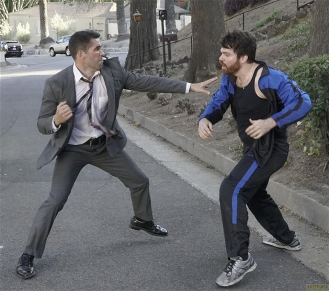 Un uomo in abito e uno in abbigliamento sportivo combattono in strada.