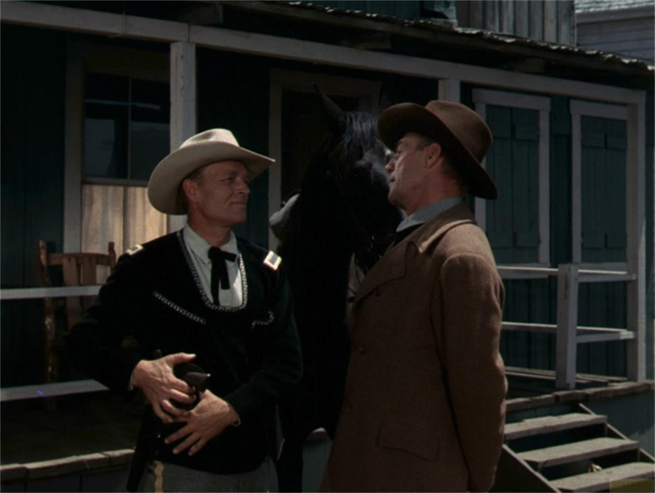 Deux hommes en chapeau de cowboy devant un bâtiment. L'un porte un uniforme.