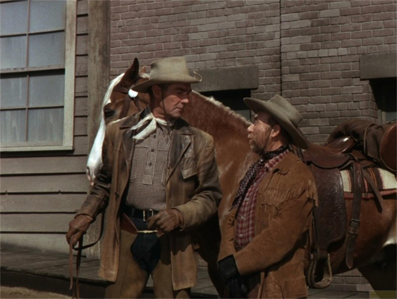 Deux cow-boys se tiennent à côté d'un cheval. L'un porte une veste en cuir, l'autre en daim à franges.