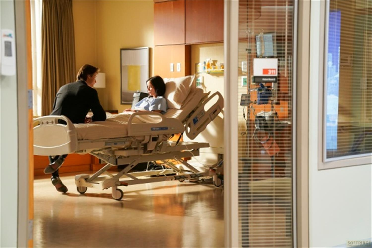 Un uomo in abito nero parla con una paziente sdraiata in un letto d'ospedale.