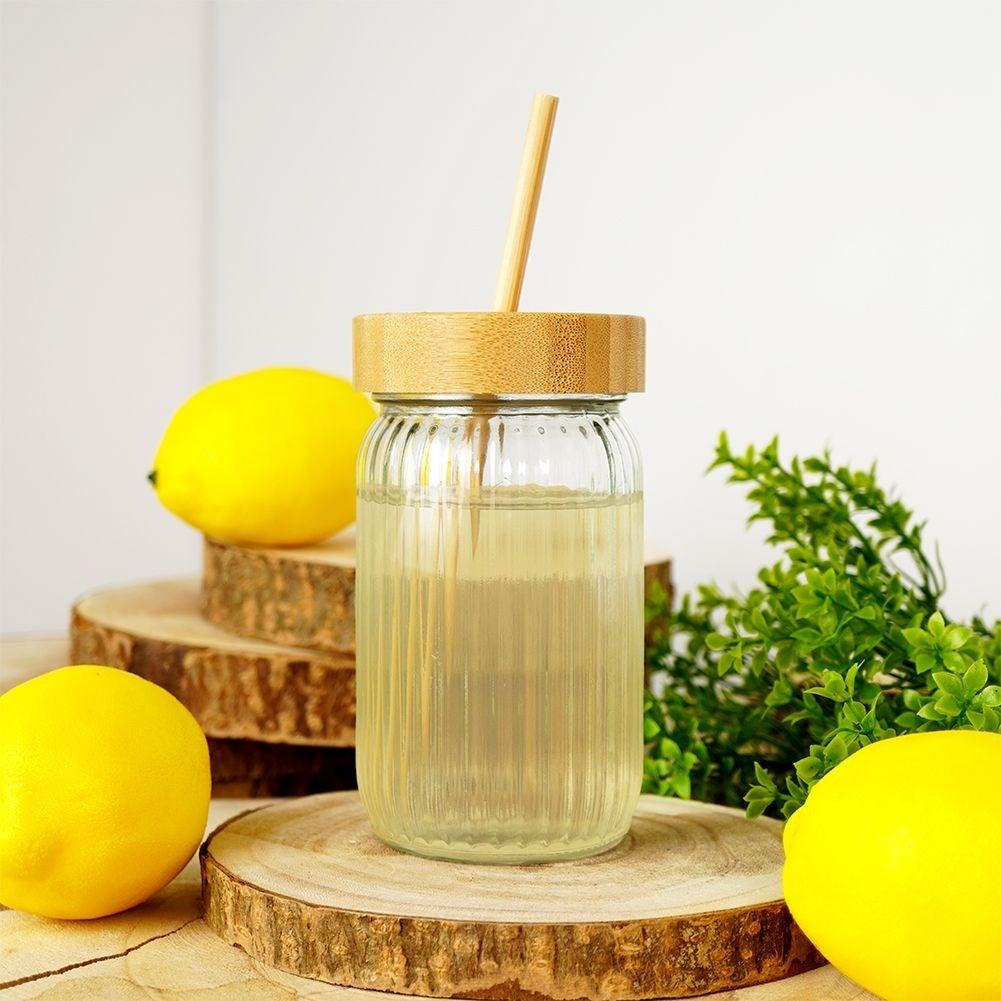 Un frasco con bebida y pajita, rodeado de limones y vegetación sobre rodajas de madera.